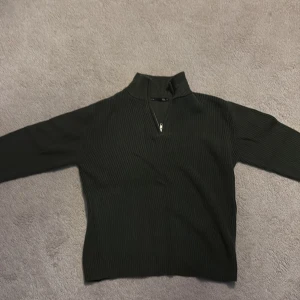 Svart ribbad tröja med half zip - Svart ribbad tröja från H&M med hög krage och half zip-dragkedja framtill. Tröjan har lång ärm och är i ett stretchigt, stickat material som sitter snyggt på kroppen. Perfekt för lager-på-lager och stilrena outfits.
