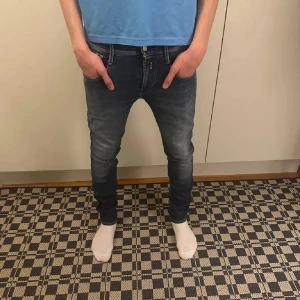 Mörkblå skinny jeans med broderade fickor - Säljer ett par mörkblå skinny jeans med snygga broderade bakfickor och klassisk femficksdesign. Jeansen har låg midja och är tillverkade i stretchigt denim för en tight passform. Perfekta för dig som gillar en modern och slimmad look.