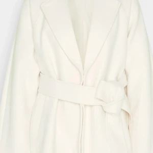 Vit omlott kappa med bälte - Snygg vit kappa från Gina med breda slag, omlottstängning och matchande bälte i midjan. Jackan har långa ärmar och två fickor framtill. Perfekt och stilren modern kappa till höst och vår. Kan även användas under vinter med tjockare tröja under. 