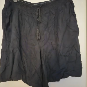 Svarta shorts med snörning från Xlnt - Säljer ett par svarta, luftiga shorts från Xlnt i storlek 2XL. De har elastisk midja med snörning och är tillverkade i 100% viskos, vilket gör dem riktigt sköna och svala. Perfekta för varma dagar och chill vibes.