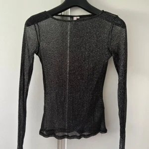 Glittrig mesh topp från Nelly - Säljer en svart glittrig mesh topp från Nelly i storlek S. Toppen är långärmad, tight och har en transparent look med glittriga detaljer i tyget. Perfekt vid finare tillfällen. Själv har jag använt den en gång. 