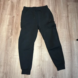 Svarta Nike Tech - svarta nike tech byxor, i storlek S herr. Helt nytt skick 