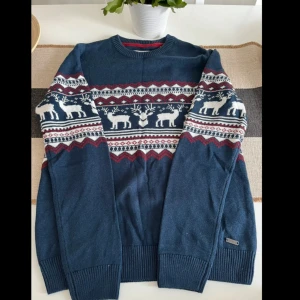 Blå stickad jultröja från edc - Mysig blå stickad tröja från edc med klassiskt julmönster i vitt och vinrött. Tröjan har rund hals, långa ärmar och motiv med renar och grafiska detaljer runt bröst och ärmar. Perfekt för vinterns alla chilliga dagar.helt ny.