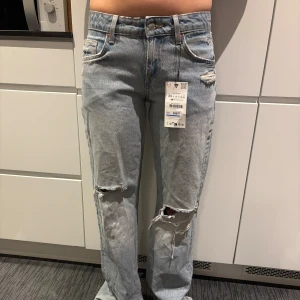 Zara wide leg low waist  jeans med slitningar. Slutsålda!  - Ljusblå jeans från Zara i wide leg-modell med låg midja och full längd. Byxorna har slitningar vid knäna och en avslappnad passform. Perfekta för dig som gillar en trendig och avslappnad stil.Modellen på bilder är 162cm lång. Säljes pga lite för liten strl och missade att lämna tillbaka i tid. Nu slutsålda hos Zara. Lågmidjade.