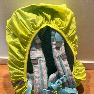 Beckmann ryggsäck med kattmotiv - Supergullig Beckmann ryggsäck i ljusblått med blommigt mönster och söt katt på framsidan. Flera fack, vadderade axelremmar och reflexdetaljer. Regnskydd i neon-gult medföljer. Perfekt för dig som vill ha en färgglad och praktisk väska till skolan.