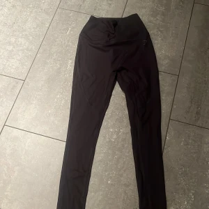 Svarta ribbade leggings från Gymshark XS - Svarta ribbade leggings från Gymshark i body fit-modell. De är höga i midjan och har en tight passform som sitter snyggt på kroppen. Materialet är en blandning av nylon och elastan, vilket gör dem stretchiga och bekväma för träning. Diskret Gymshark-logga på benet. Ordinarie pris är cirka 400 kronor. Priset kan diskuteras vid snabba affärer.