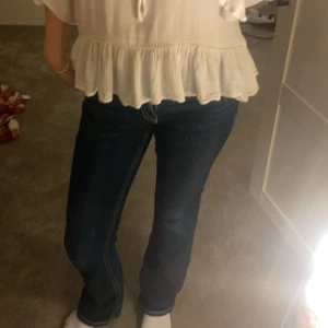 Mörkblå bootcut jeans från Gina young - Säljer ett par mörkblå jeans med bootcut-modell och vita kontrastsömmar. Byxorna har låg midja och snygga fickdetaljer med knapp bak. Klassisk jeanslook som passar till det mesta och ger en schysst siluett.