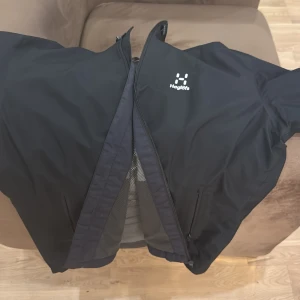 Svart vindjacka från Haglöfs - Säljer en svart vindjacka från Haglöfs med stilren design och diskret logga på bröstet. Jackan har dragkedja framtill, två sidofickor med dragkedja och meshfoder på insidan. Perfekt för blåsiga dagar och outdoor-aktiviteter. Den är oanvänd helt ny och goretex som är vattentät och är en material som är speciell och dyr köpte den för 4000kr har kvitto 