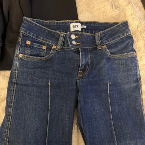 Mörkblå jeans från 157 Paris Crease - Mörkblå jeans med vida ben från 157 Paris Crease. Klassisk femficksmodell med kontrastsömmar, dubbla knappar i midjan och markerad pressveck längs benen. Snygg och enkel design som passar till det mesta. Materialet är klassisk denim. Låg midja!