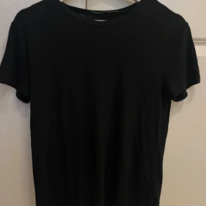 Svart t-shirt från 157, storlek M - En stilren svart t-shirt från 157 i storlek M. Klassisk rund hals och korta ärmar, perfekt för en enkel och clean look. Tillverkad i mjuk bomull som känns skön mot huden. Passar dig som gillar minimalistisk stil.