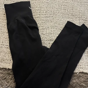 Svarta ribbade leggings - Svarta leggings med diskret ribbad struktur och stretchigt material. Perfekta för en chill och bekväm stil, passar till både oversized hoodies och crop tops. Liten logga upptill vid midjan.