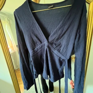Mörkblå omlottopp - Säljer en mörkblå omlottopp från Gina med v-ringning och långa ärmar. Toppen har knytband i midjan och är tillverkad i ett lätt, strukturerat material💕 knappt använd