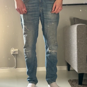 Ljusblå slitna jeans från G-Star - Säljer ett par ljusblå jeans från G-Star med snygga slitningar och hål på benen. Jeansen har raka ben, klassiska fem fickor och coola detaljer på bakfickorna. Perfekt för dig som gillar en avslappnad och trendig look.