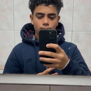 Mörkblå hoodie från Burberry - Säljer en mörkblå hoodie från Burberry med klassiskt rutigt mönster i huvan. Tröjan har snörning vid huvan och ett broderat Burberry-logo på bröstet. Perfekt för dig som gillar stilren design med en touch av lyx.