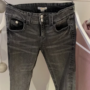 Grå jeans från Gina Tricot, storlek 158 - Snygga grå jeans från Gina Tricot med slitningseffekt och dubbla silverknappar i midjan. Modellen har klassiska fickor fram och bak, samt bälteshällor. Jeansen är i stretchigt material och har en smal passform som sitter snyggt.