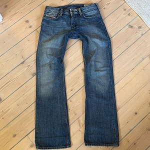 Diesel Zatiny blå jeans W28 L32 - Snygga blå jeans från Diesel, modell Zatiny. Klassisk femficksdesign med raka ben och diskreta slitningar. Jeansen har en mörkblå tvätt och detaljerade sömmar, tillverkade i robust denim. Perfekta för dig som gillar en tidlös och stilren look.