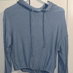 Blå ribbad hoodie med snörning - Säljer en ljusblå ribbad hoodie med huva och snörning både vid halsen och nederkanten. Tröjan har långa ärmar och är tillverkad i ett mjukt, stickat material som ger en chill och avslappnad vibe.