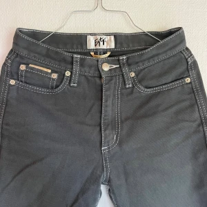 EYTYS jeans  - Snygga svarta jeans från Eytys med vita kontrastsömmar och klassisk femficksdesign. Modellen har bootcut-ben och hög midja, vilket ger en riktigt clean och trendig siluett. Perfekta för dig som vill sticka ut med en cool och modern look.