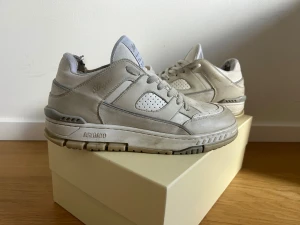 Axel Arigato vita sneakers i skinn - Säljer ett par chunky vita sneakers från Axel Arigato med perforerade detaljer och broderad logga på sidan. Skorna har snörning, robust sula och är tillverkade i skinn med textilfoder. Perfekta för dig som gillar stilrena och sportiga vibes.