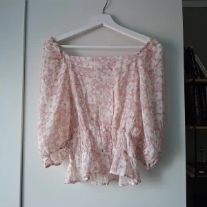 Blommig blus från Rut&Circle XS - Säljer en söt blommig blus från Rut&Circle i storlek XS. Blusen är ljusrosa och vit med volangkant nedtill och puffiga långärmar. Den har en offshoulder-design och är gjord i ett lätt, luftigt material! 