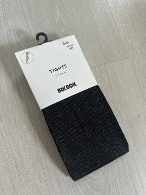 Svarta glittriga tights från BikBok - Svarta tights/strumpbyxor från BikBok med glittriga detaljer som ger en snygg touch. Tightsen är i storlek S-M och helt nya i originalförpackning, ordinarie pris 129 kr