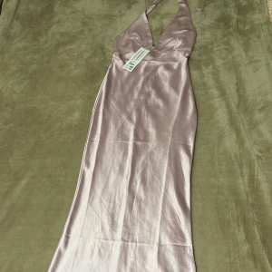 Ljusrosa långklänning i satin - Supersnygg långklänning från Gina Tricot i ljusrosa satin. Klänningen har halterneck, djup v-ringning och en elegant, slät siluett. Perfekt för dig som vill sticka ut med en stilren och trendig look.