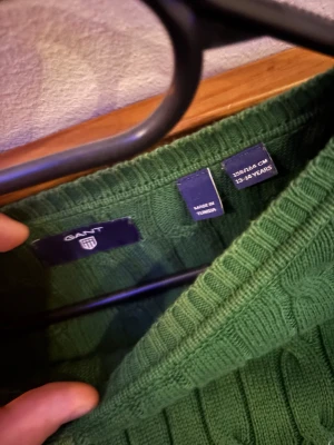 Grön kabelstickad tröja från GANT - Snygg grön kabelstickad tröja från GANT med klassisk rund halsringning och broderad logga på bröstet. Tröjan har långa ärmar och är tillverkad i mjukt stickat material som passar perfekt för kyligare dagar.