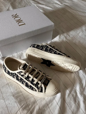 Dior walk N dior - ÄKTA. PRIS KAN DIKSUTERAS! Snygga Dior Oblique sneakers med blått och beige mönster, klassisk snörning och rund tå. Skorna har en platt sula med stjärndetalj undertill och tydlig Christian Dior-logga på både plös och häl. Tillverkade i canvas med exklusiv känsla.