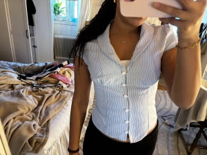 Blårandig kortärmad skjorta med knappar - Snygg kortärmad skjorta med smal passform och klassisk krage. Skjortan har vita och blå ränder, knappar hela vägen framtill och lätt v-ringad hals. Perfekt för dig som gillar en fräsch och stilren look. Materialet känns som bomull och är bekvämt mot huden. Aldrig använd!