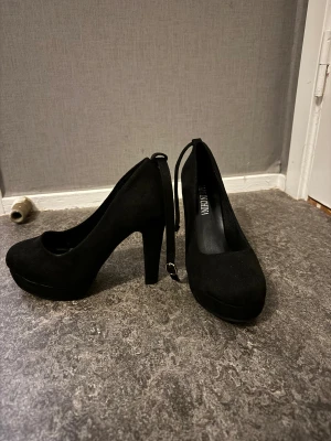 Svarta klackar - Snygga svarta pumps med hög klack och platåsula. Skorna har rund tå och är klädda i mockaliknande material. Enkla och stilrena med smal rem baktill som ger en extra detalj. Aldrig använt. Ordinare pris 165kr 🌸 