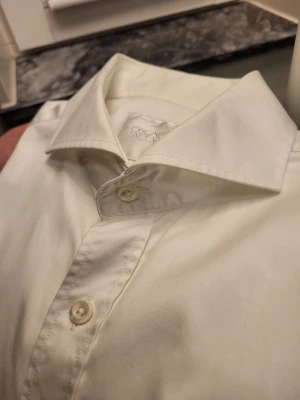 Vit slim fit skjorta Oscar Jacobson 42 - Vit skjorta från Oscar Jacobson i storlek 42, modell Herman slim shirt. Skjortan är tillverkad i tvålagers bomull och har klassisk krage, långa ärmar och knappar framtill. Snygg och stilren passform som sitter tajt över kroppen.