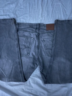 Grå jeans från Jack & Jones - Säljer ett par grå jeans från Jack & Jones med relaxed passform. Klassisk femficksmodell med knappgylf och bälteshällor. Jeansen har en rak siluett och är tillverkade i slitstarkt bomullsjeansmaterial. Perfekt för dig som gillar en avslappnad stil. Är lite mer bagy men väldigt snygga och stilrena 