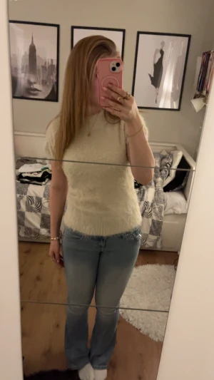 Ljus fluffig stickad topp med rosett - Superfin ljusbeige stickad topp med korta ärmar och hög krage. Mjuk och fluffig känsla, med en stor rosett i satin baktill som ger en extra söt touch. Perfekt för dig som gillar unika detaljer och vill ha något som sticker ut. Egenfixad satinknytning