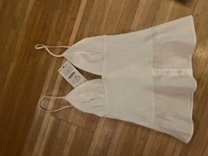 Vit ribbad linnetopp med knappar - Säljer en fräsch vit linnetopp från Zara i storlek S. Toppen har smala axelband, ribbad mittdel och knappar framtill. Den är figurnära upptill och har en lätt utsvängd nederdel. Perfekt för dig som gillar stilrena och trendiga plagg.