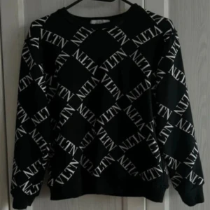 Svart sweatshirt från Valentino - Svart sweatshirt från Valentino med VLTN-logga i vitt tryckt över hela tröjan i ett rutigt mönster. Den är äkta och i jätte bra skick.