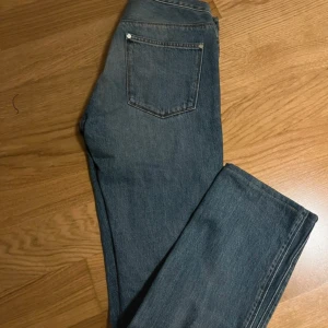 Blå jeans från Acne Studios 32/32 - Snygga blå jeans från Acne Studios i klassisk straight/slim fit Modellen har fem fickor, normal passform och är tillverkad i 100% bomull. Jeansen har en mörkblå tvätt med subtila slitningar och orangea sömmar. Perfekt för dig som gillar stilrena och tidlösa jeans.ä nypris är ca 4500kr, skriv vid frågo, priset går att diskutera vid snabb affär!