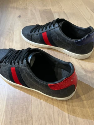 Gucci Ace svarta  - Svarta Gucci Ace i väldigt bra skick. Storleken är 43 men passar även 42. Orginalbox och dustbag följer med. Priset är inte helt hugget i sten så hör av dig vid intresse.