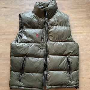 Olivgrön dunväst från Polo Ralph Lauren - Hej! Säljer en olivgrön dunväst från Polo Ralph Lauren med klassisk röd logga på bröstet. Perfekt att slänga över en hoodie för extra värme. Använd förra hösten, skickas eller hämtas i Umeå 😃