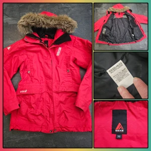 Röd parkajacka från 8848 Altitude - Säljer en röd parkajacka från 8848 Altitude med fuskpäls på huvan och svarta detaljer. Jackan har dragkedja och knappar framtill, flera fickor och justerbar midja. Materialet är polyester och fodret är svart. Perfekt för kalla dagar.
