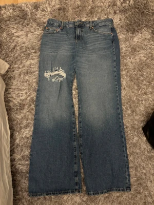 Blå wide jeans från Perfect Jeans - Säljer ett par blå jeans från Perfect Jeans i storlek 38. Modellen är wide med raka ben och har en snygg sliten detalj med hål på ena låret. Klassisk femficksdesign och låg midja. Helt oanvända 