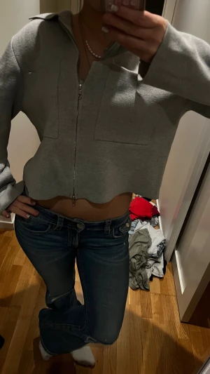 Grå croppad overshirt med dragkedja - Säljer en stilren grå croppad overshirt med dragkedja framtill och bred krage. Jackan har långa ärmar och en loose passform som ger en chill vibe. Perfekt att slänga på över en t-shirt eller linne för en enkel och snygg look.