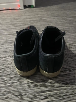 Svarta Lanvin sneakers med lackad tå - Säljer ett par svarta Lanvin sneakers med snygg lackad tå och snörning. Ovandelen är i mocka och detaljer i skinn, med vit platt sula. Klassisk rund tå och stilren design som passar till jeans eller dressat. Märket syns på sulan. Riktigt schyssta sneakers för dig som gillar exklusiva märken.