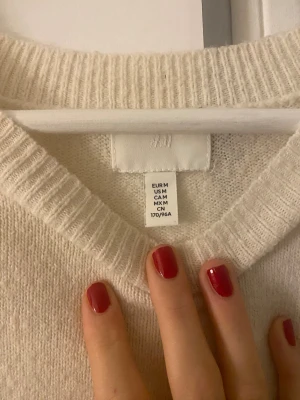Krämvit  stickad tröja  - Säljer en enkel och snygg krämvit stickad tröja från H&M i storlek M. Tröjan har rund hals, långa ärmar och breda ribbade muddar vid ärmslut och nederkant. Finns ett litet hål men syns ej om du har håret i vägen 