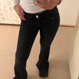 Svarta bootcut jeans med detaljer - Säljer ett par trendiga, lågmidjade bootcut-jeans i toppskick! Jeansen sitter riktigt snyggt på kroppen, midjan är låg och landar precis under naveln för den där perfekta Y2K-looken. Tyvärr är de lite för långa för mig, annars hade jag behållit dem utan tvekan!  Perfekta för dig som vill ha ett par riktigt stilrena och trendiga jeans med det lilla extra. 