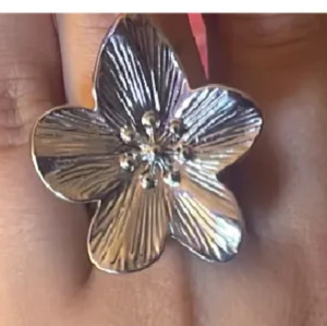 Stor silverfärgad blomring - Unik ring i form av en stor blomma med detaljerade ådringar och små kulor i mitten. Ringen är i silverfärg och har en iögonfallande design som verkligen sticker ut. Perfekt för dig som vill ha ett smycke som syns och ger en cool touch till din stil.