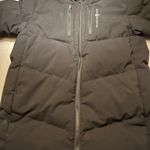 Svart pufferjacka Sail Racing - Svart pufferjacka från Sail Racing med huva. 8/10 i skick bara använd 3 gånger. Ny pris 3500 mitt pris 1000. Storlek 168 13-14 år.  Hör av er om ni har några frågor!