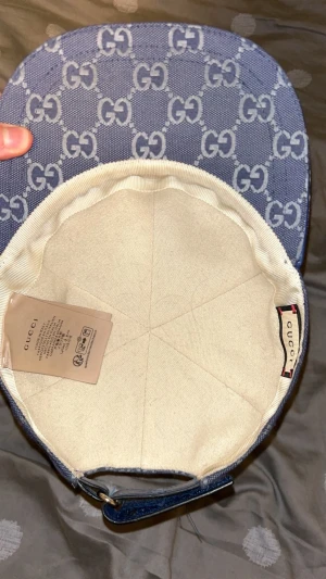 Blå Gucci keps med GG-mönster - Snygg blå keps från Gucci med klassiskt GG-mönster över hela kepsen. Justerbar rem baktill i blått och insida i beige bomull. Perfekt för dig som vill ha en lyxig och trendig accessoar med streetkänsla.