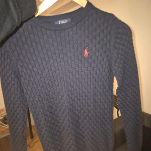Mörkblå stickad tröja Polo Ralph Lauren - Snygg mörkblå stickad tröja från Polo Ralph Lauren med diskret rutmönster och röd broderad logga. Väldigt bra skick.