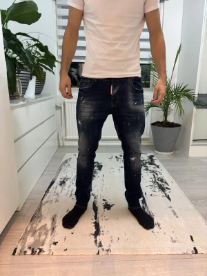 Dsquared2 blå slitna jeans - Säljer ett par blå jeans från Dsquared2 med coola slitningar, färgstänk och broderade detaljer. Jeansen är i storlek 52 i dsquared storlekar vilket innebär att dem passar folk som har 34 -34. Dem är inte heller för thigta och dem sitter fint på om man har några frågor om storlekarna är det bara att kontakta 