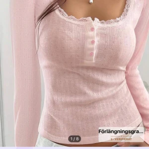 Ljusrosa långärmad topp - Supersöt ljusrosa långärmad topp med ribbad struktur och små hålmönster. Urringningen är dekorerad med spets och har fyra rosa knappar framtill. Toppen är figurnära och har en feminin, romantisk vibe som passar perfekt till jeans eller kjol. Tröjan har ett pytte litet hål i sidan men syns inte och lätt att sy igen